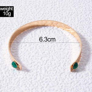 Detail view of gold hammer texture open bracelet with green teardrop gemstones