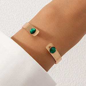 Detail of gold-plated cuff bracelet featuring dual emerald green stones on a female wrist