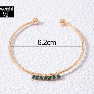 Detail of golden bangle with seven green gemstones and 6.2cm inner diameter