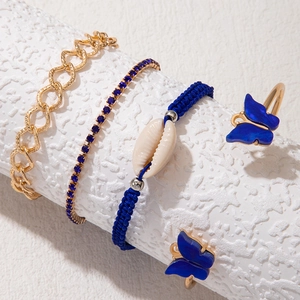 Détail de bracelets dorés avec breloques papillon bleu et accents de coquillages bohèmes