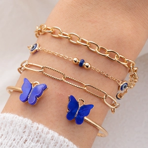 Ensemble de quatre bracelets dorés avec breloques papillon bleu et détails mauvais œil