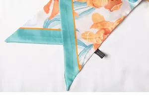 Detalle de costura azul y estampado floral naranja en bufanda de seda blanca twilly