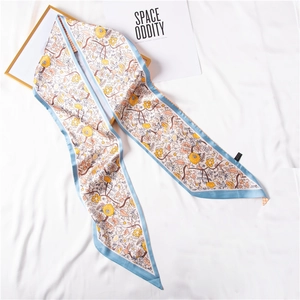 Elegant silk-like scarf with yellow floral print and blue trim on a white fabric background