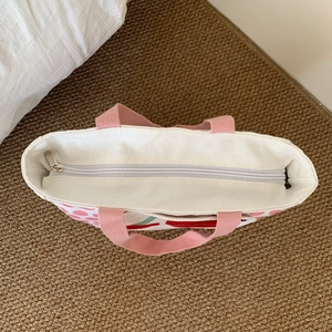 Detail view of white canvas insulated lunch bag with pink handle and top zipper closure