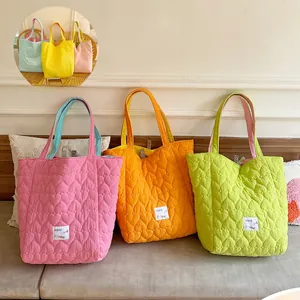 Detail of candy-colored heart-quilted tote bags featuring reversible sides and embroidered text
