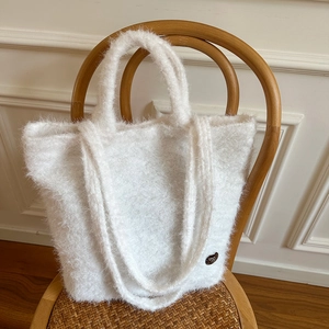 Detail of soft white plush tote bag texture and design on a minimalist wooden chair