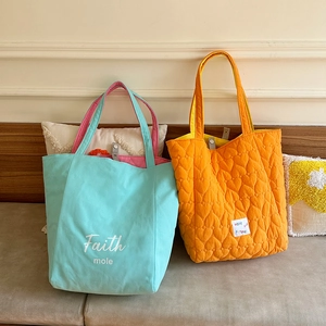 Close-up of mint green and orange quilted tote bags with vibrant contrasting linings