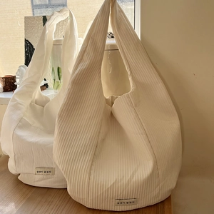 Detailed view of the vertical pleated texture and woven label on a cream white tote bag