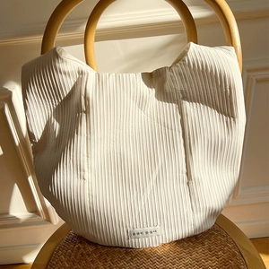 Detail of off-white pleated tote bag with vertical stripes and round wooden handle