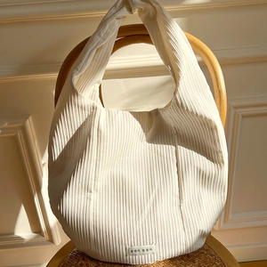 Close-up of pleated cream shoulder bag with fabric label on a vintage rattan chair