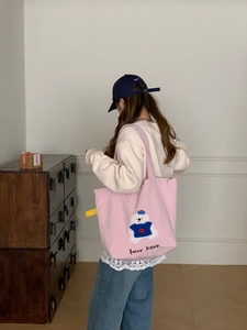 Detailed bear embroidery on a pink canvas tote bag carried by a model in a home setting