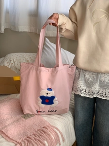 Detail of pink canvas tote bag showing embroidered teddy bear in blue sweater and text