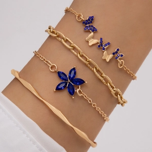 Détail d'un ensemble de quatre bracelets dorés avec breloques papillon et fleurs bleues