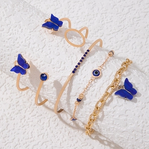 Détail du parure de bijoux cinq pièces avec papillons bleus et bracelets dorés multicouches