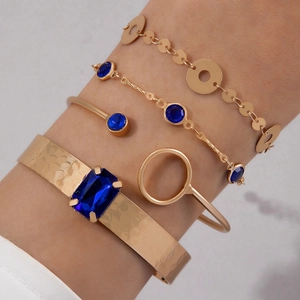 Détail de bracelets superposés dorés avec des pierres bleues et des joncs métalliques texturés