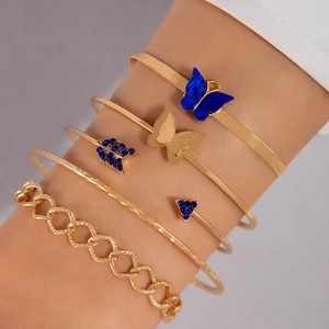Détails de bracelets dorés superposés avec pendentif papillon bleu et motifs géométriques
