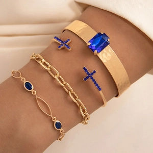 Détail d'un ensemble de quatre bracelets dorés avec gemmes bleu foncé et charms croix