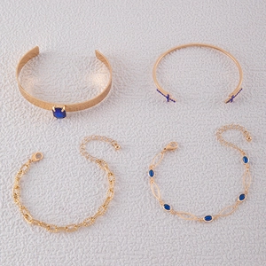 Vue à plat d'un ensemble de 4 bracelets dorés avec pierres bleues et designs évidés