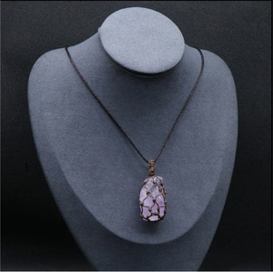 Détail d'un pendentif en cristal violet naturel avec pochette en maille marron tissée