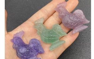 Detailed close-up of three hand-carved fluorite rooster figurines in purple and green