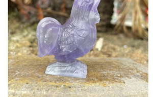Macro side view of purple translucent crystal rooster figurine with carved feather details