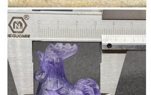 Macro view of a purple crystal rooster carving being measured with a digital caliper