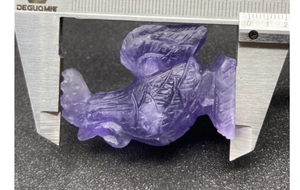 Macro detail of hand-carved purple fluorite rooster figurine measured with a caliper