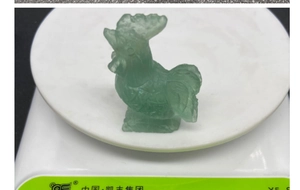 Detailed close-up of a hand-carved green fluorite rooster sculpture on a scale