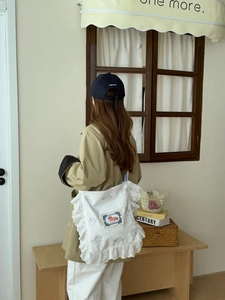 Détail d'un sac en toile blanche avec bordure en dentelle et motif ange porté par un mannequin