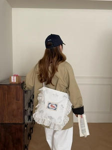Détail du sac à bandoulière en toile blanche avec bordure dentelle et motif ange