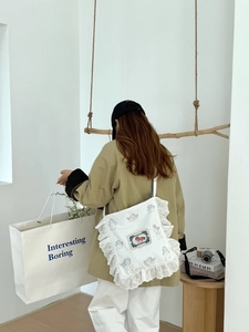 Détail du sac en toile blanche avec bordure en dentelle, motif ange et patch vintage