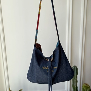 Dettaglio borsa hobo in denim con tracolla floreale e ricamo con caratteri