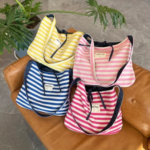 Gros plan de sacs cabas en toile rayés avec broderie SEE YOU sur un canapé en cuir