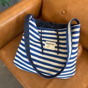 Détail du sac cabas en toile rayé bleu et blanc avec broderie SEE YOU sur canapé en cuir
