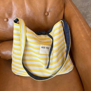 Détail du sac en toile rayé jaune et blanc avec écusson brodé See You sur le canapé
