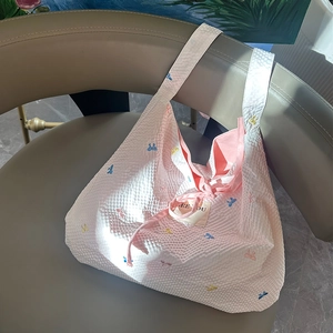 Détail du sac cabas en maille gaufrée rose clair avec broderies de nœuds colorés et lien