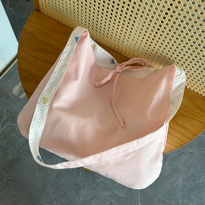 Détail du sac fourre-tout rose en toile avec bordure florale et cordon sur chaise en rotin