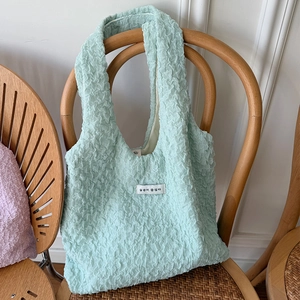 Dettaglio borsa shopper verde menta in tessuto goffrato su una sedia di vimini
