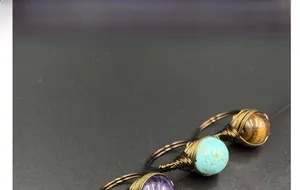 Detail of three handmade wire-wrapped gemstone rings in amethyst, turquoise, and tiger eye