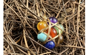 Detailed view of handmade gold wire-wrapped chakra gemstone pendant on rustic wood