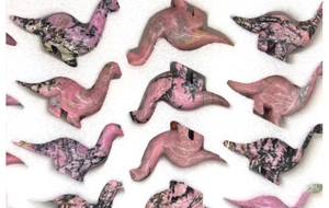 Detailed view of hand-carved pink rhodonite crystal dinosaur figurines in protective foam