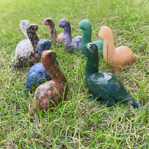 Polished natural stone dinosaur carvings in various crystals and gemstones on green grass