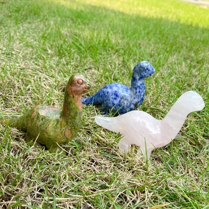 Three-piece set of polished dinosaur crystal carvings on a green natural grass background