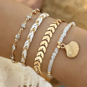 Close-up of Bohemian layered bracelets with gold leaf charms and shell pendants