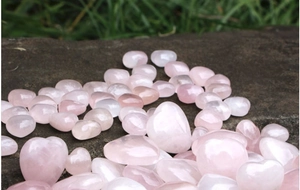 Macro di cuori in quarzo rosa lucido e ciottoli su una superficie di roccia naturale scura