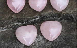 Pietre di quarzo rosa naturale a forma di cuore lucidate esposte su una superficie in pietra grigia