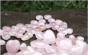 Cuori e ciottoli di quarzo rosa naturale lucidato su roccia scura, ideali per cristalloterapia