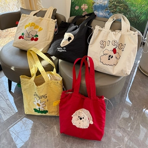 Detalle de bolsos tote de lona coloridos con bordados de dibujos y cierre de cordón ajustable