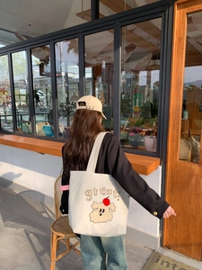 Detalle del bolso tote de lona blanca con bordado de rizo de un lindo cachorro y una manzana