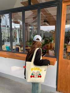 Detalle de un bolso tote de lona beige con bordado Poppy amarillo y gráficos de dibujos